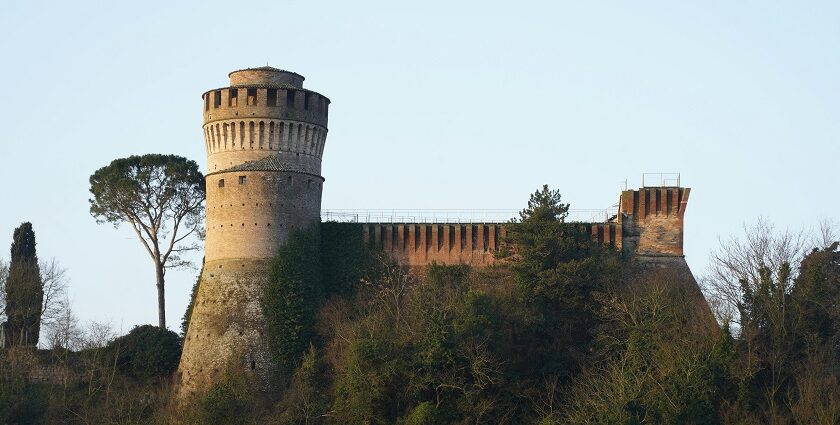 Majestic tower and castle perched on a hill, surrounded by lush greenery and a clear blue sky