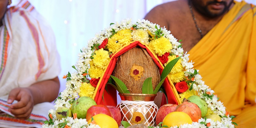 Pooja thali with traditional ritual items, including kalash, red threads and a sweet.