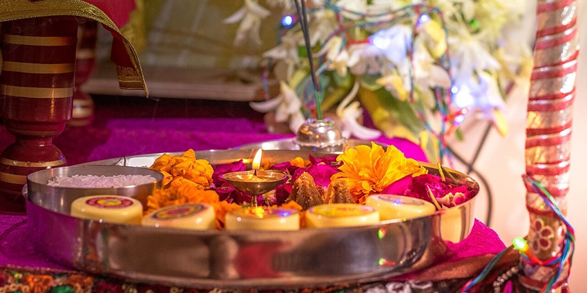 Imge of a Hindu pooja thali decorated with flowers, incense sticks and other ritual items
