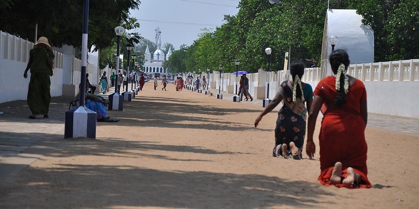 People walking and kneeling in devotion along a pathway towards the Velankanni Temple.