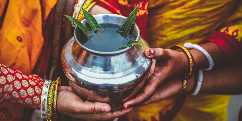 Hands of women in traditional attire holding the silver kalash with leaves in water for ritual