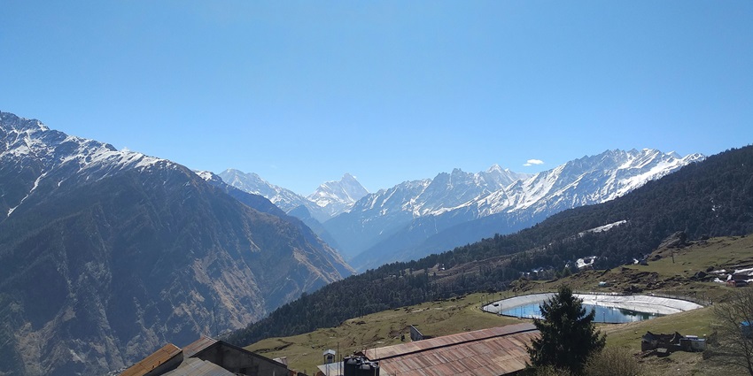 Brown and white house near green trees with mountains and a clear blue sky in the background