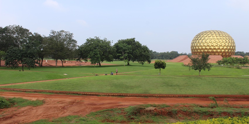 Matrimandir, a large golden sphere, set in lush green lawns and red pathways in Auroville.
