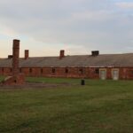 Auschwitz-Birkenau State Museum with barracks and old structure surrounded by greenery.