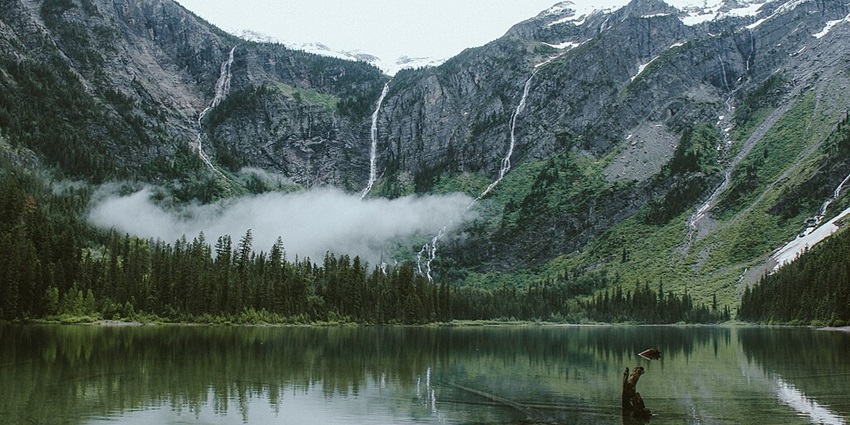 Enchanting image of the green mountains with misty clouds surrounding the Avalanche Lake