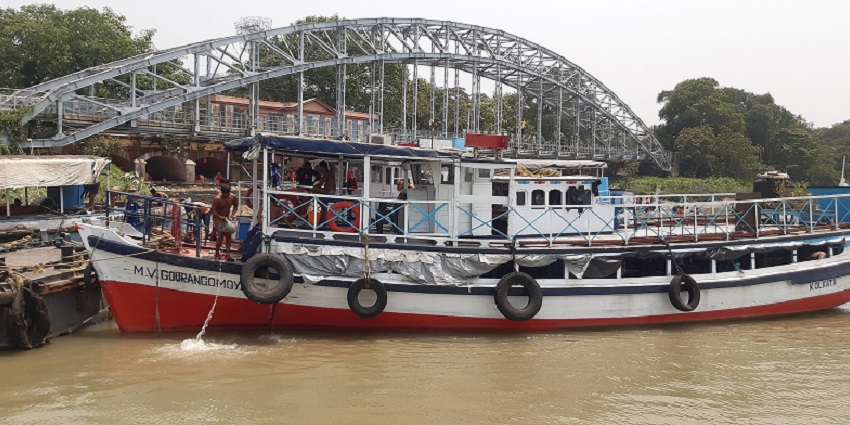 A view of the Babughat featuring a majestic bridge, a boat, and glistening blue waters.