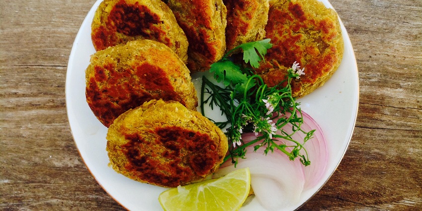 A top view of six shami kebab pieces placed on a white plate with onion and lemon slices