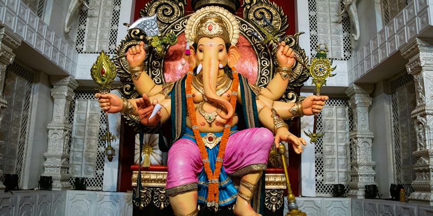 A picture of a tall idol of Lord Ganesha at a temple, decorated with garlands
