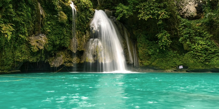 A beautiful view of a green landscape with waterfalls surrounded by rocky cliffs.