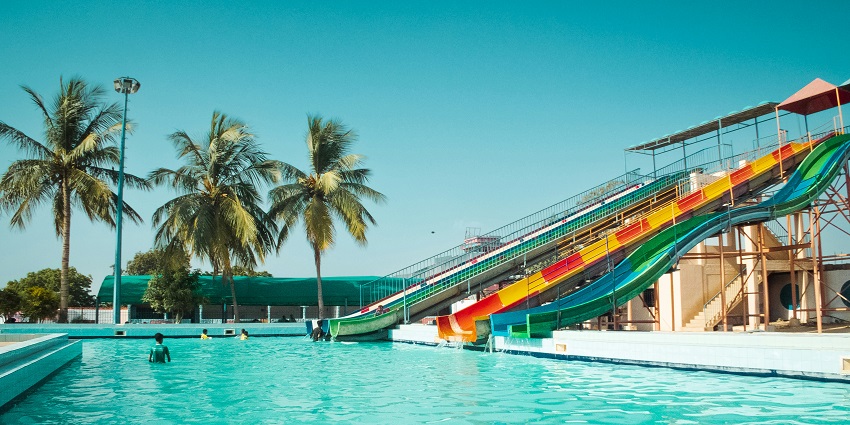A relaxing poolside in a water park featuring vibrant coloured slides at the far end