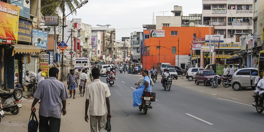 Busy street scene with pedestrians, motorcycles, and colourful buildings in an urban area.