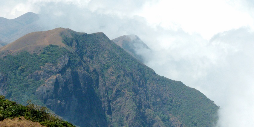 A breathtaking view of Mukurthi Cliffs, showcasing rugged terrain and lush greenery under a clear sky.