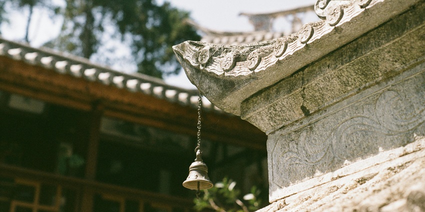 Ornate bell hanging from a wooden roof, with intricate details, set against a bright