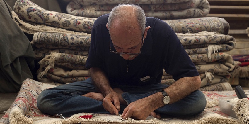 A picture of an old man arranging the carpets that he has put out for selling
