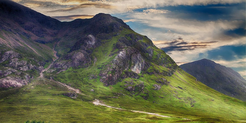 A landscape featuring green hills and a mountain range under a bright blue sky.