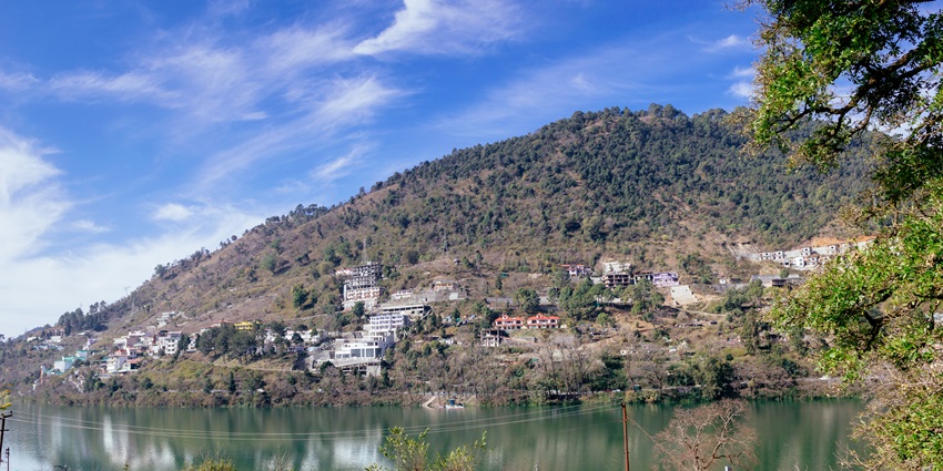 Serene view of forest-covered hills reflected in the calm waters of Bhimtal Lake in Uttarakhand, one of the best places to visit in Uttarakhand in October.