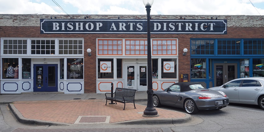 The entrance of the Bishop Arts district with cars parked and a bench beside a street lamp