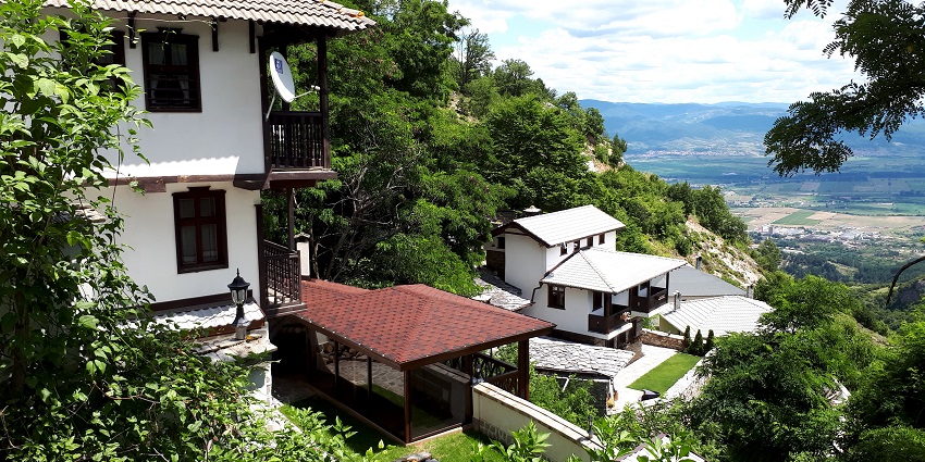 Blagoevgrad town with houses, surrounded by greenery, mountains and farms on plain.