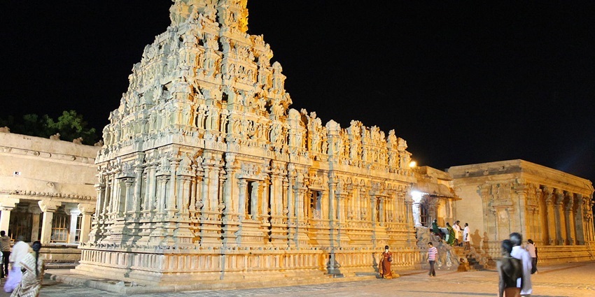 A cream-white-coloured ancient temple at night with intricate detailing and people around.