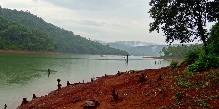 An image of Brahmand Ghat framed by large green hills which are everywhere lush.