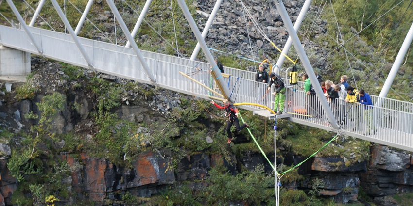 Bungee jumper mid-air from Bridge over a river valley surrounded by lush logic