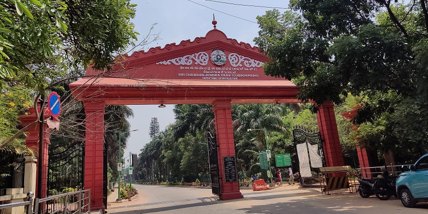 Ornate entrance gate of Cubbon Park with red pillars and lush greenery in Bengaluru.