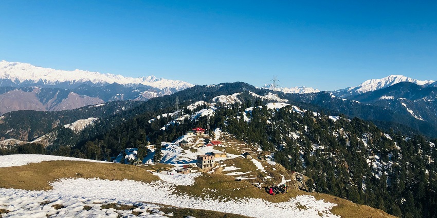 A serene view of snow-clad peaks, lush green vegetation, and rustic lands of Chamba
