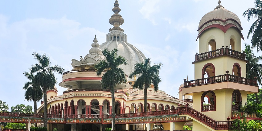A picture of a majestic Hindu Temple with a garden area and pine trees in front