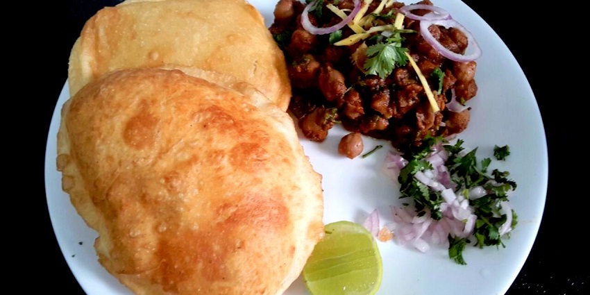 A plate of chole bhature served with lemon and onions