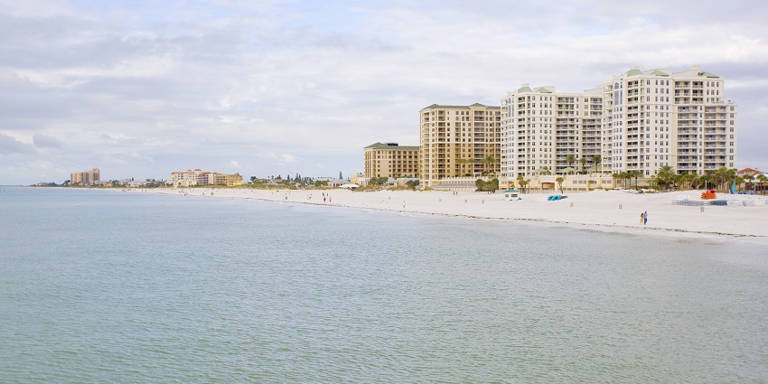 Clearwater beach with people walking on sandy shore and buildings in the background
