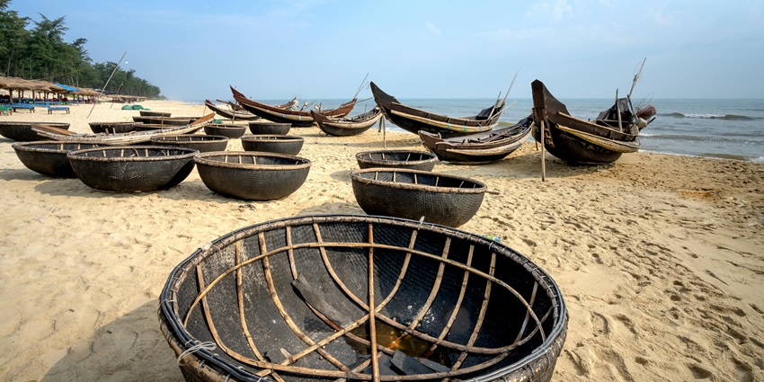 Coracles lined on a sandy ocean beach under cloudy blue sky, ready to float–kodiveri waterfalls