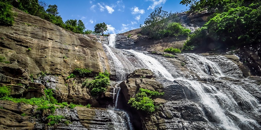 An astonishing view of the Courtallam Waterfalls surrounded by lush green vegetation.