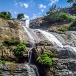 An image showing Courtallam Waterfalls cascading over rugged rocky terrain in full flow.