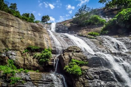 An image showing Courtallam Waterfalls cascading over rugged rocky terrain in full flow.