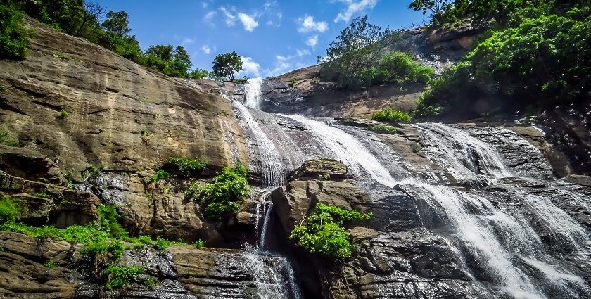 An image showing Courtallam Waterfalls cascading over rugged rocky terrain in full flow.