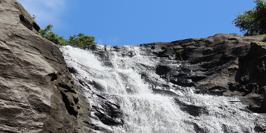 Palaya Kutralam Falls cascading down rocky slopes, surrounded by a green landscape