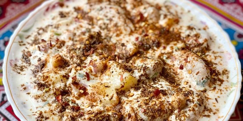 Image of a plate of Dahi-Arbi Jhor, covered with curd and spices on the top.