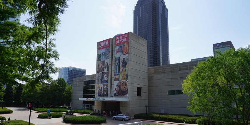 The entrance of the Dallas Museum of Art with visitors entering and cars stopping in front