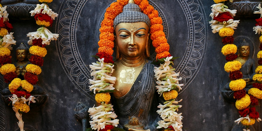 A close-up view of a Buddha statue offered vibrant pink and white flowers in a temple.