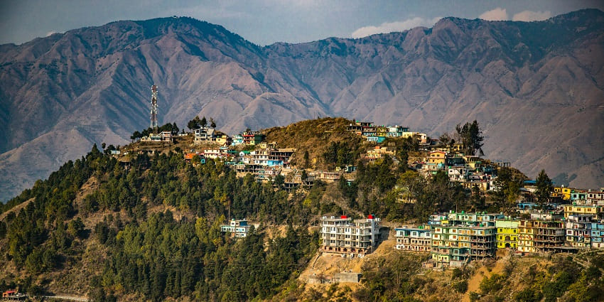 A serene view of Dhanaulti featuring majestic snow-clad mountains and a quaint town.
