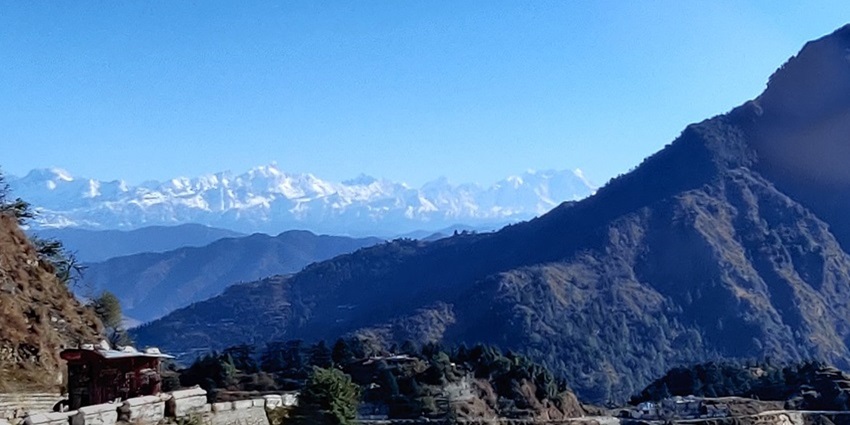 An image showing a scenic view from Dhanaulti with dense green hills and clear skies.