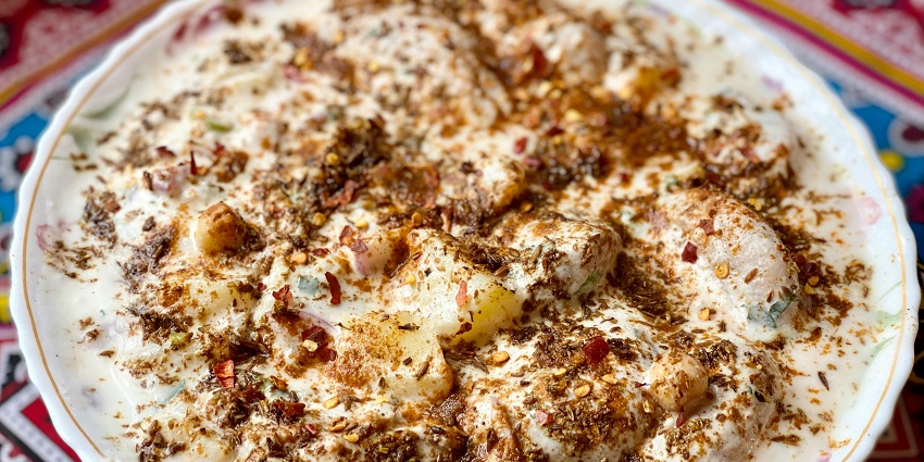 A close up view of a dahi vada containing various ingredients is served on a white plate.