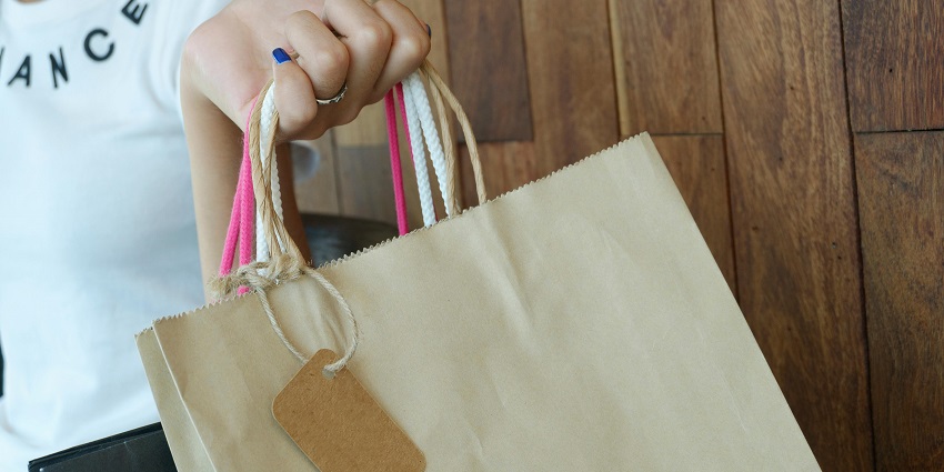 An image depicts a person holding a brown paper shopping bag while shopping, one of the things to do in Erode.
