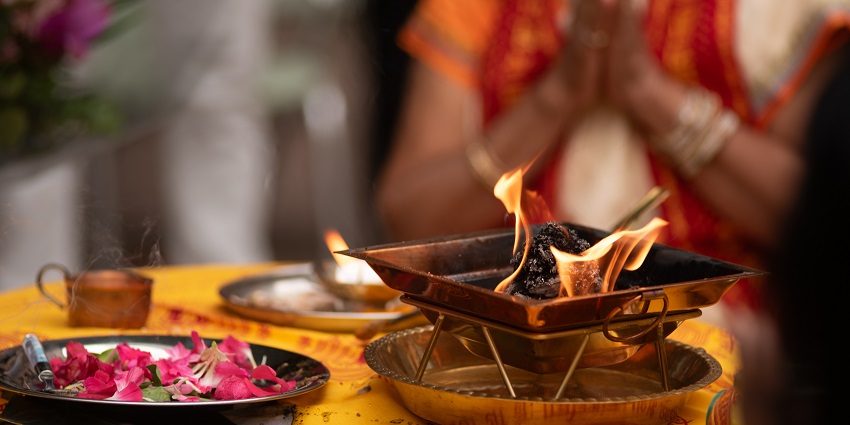 A burning tray and plate full of flowers, placed on an altar with a blurred woman praying