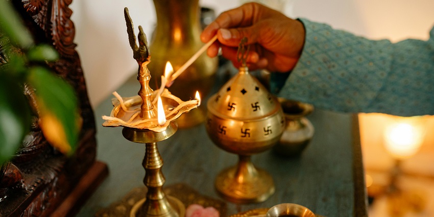 A person igniting the incense stick and a brass diya for aarti and pooja on the table.