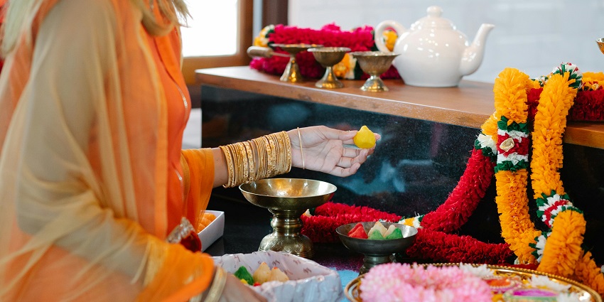 A woman decorating a place with flowers, performing a ritual with puja items around her.