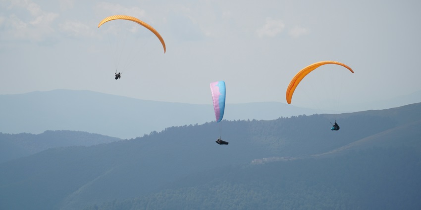 Three gliders performing paragliding over the scenic hills of Nainital under a clear blue sky.