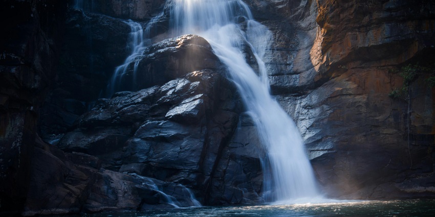 A picture of a waterfall with water cascading down the hill, taken during twilight hour