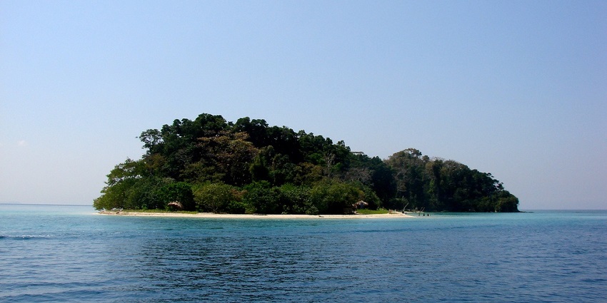 An image of a tropical island that consists of hillocks, a sandy beach, and boats.