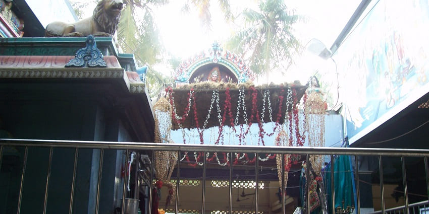 Open roof structure of Vekkaliyamman Temple decorated with flowers and a lion idol on the side.